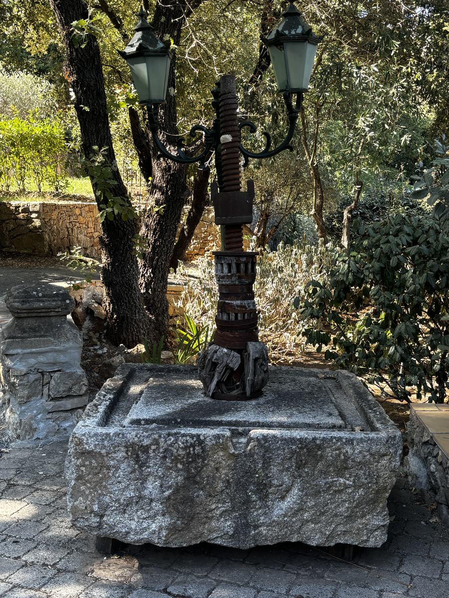 An old screw press on its stone base, in the gardens.