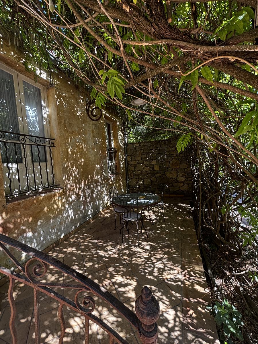A wrought-iron table beneath the wisteria, against the bastide's weathered façade.