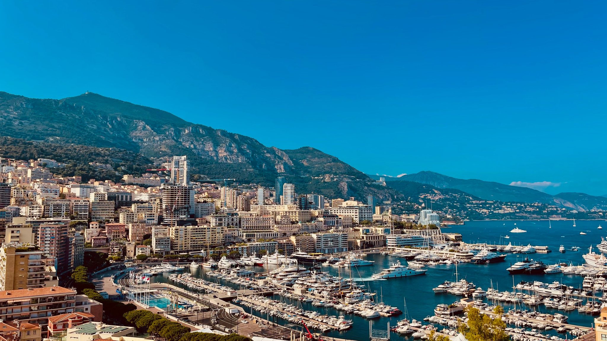 Panorama del Porto Ercole a Monaco — yacht ormeggiati, palazzi di Montecarlo e montagne sullo sfondo.