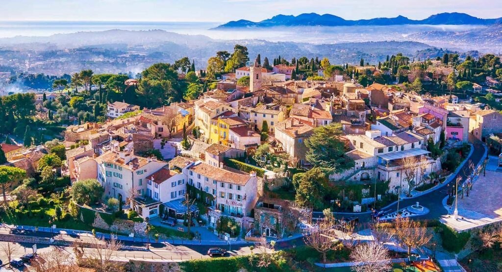 Veduta aerea del vecchio borgo di Mougins — vicoli a spirale, campanile e colline dell'Esterel sullo sfondo.