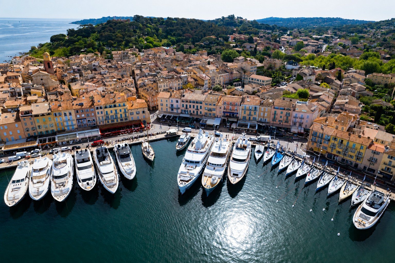 Vue aérienne du port de Saint-Tropez — yachts à quai, façades du vieux village et clocher ocre.